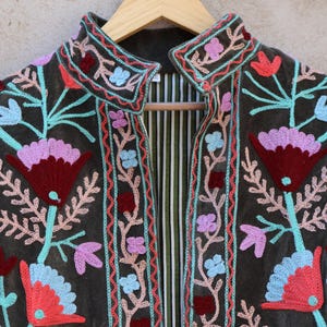 Peut inclure: Une veste en velours vert fonc&eacute; avec des broderies florales color&eacute;es. La veste a un col mandarin et une fermeture &agrave; l'avant.