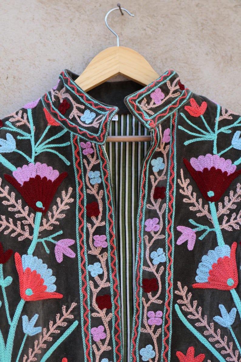 Peut inclure: Une veste en velours vert fonc&eacute; avec des broderies florales color&eacute;es. La veste a un col mandarin et une fermeture &agrave; l'avant.