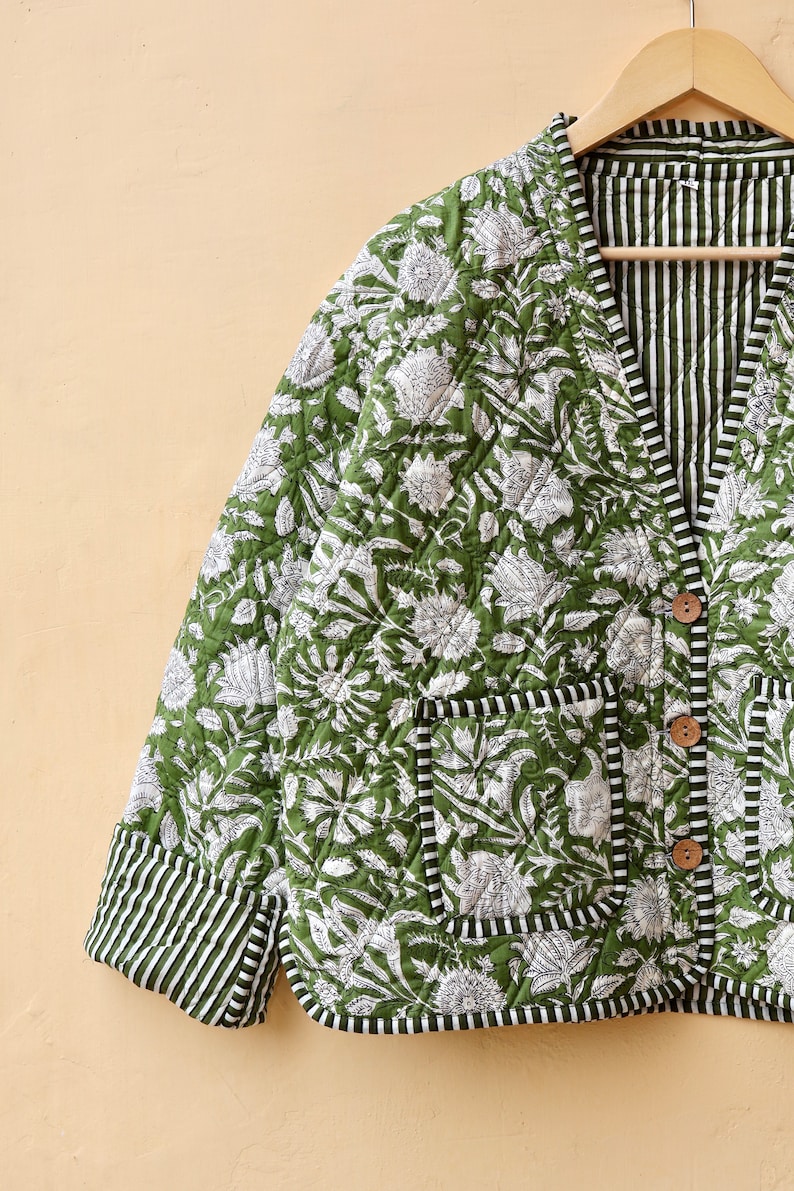 Puede incluir: Una chaqueta acolchada verde con estampado floral blanco y forro a rayas. La chaqueta tiene cierre de bot&oacute;n y un bolsillo en el lado izquierdo.