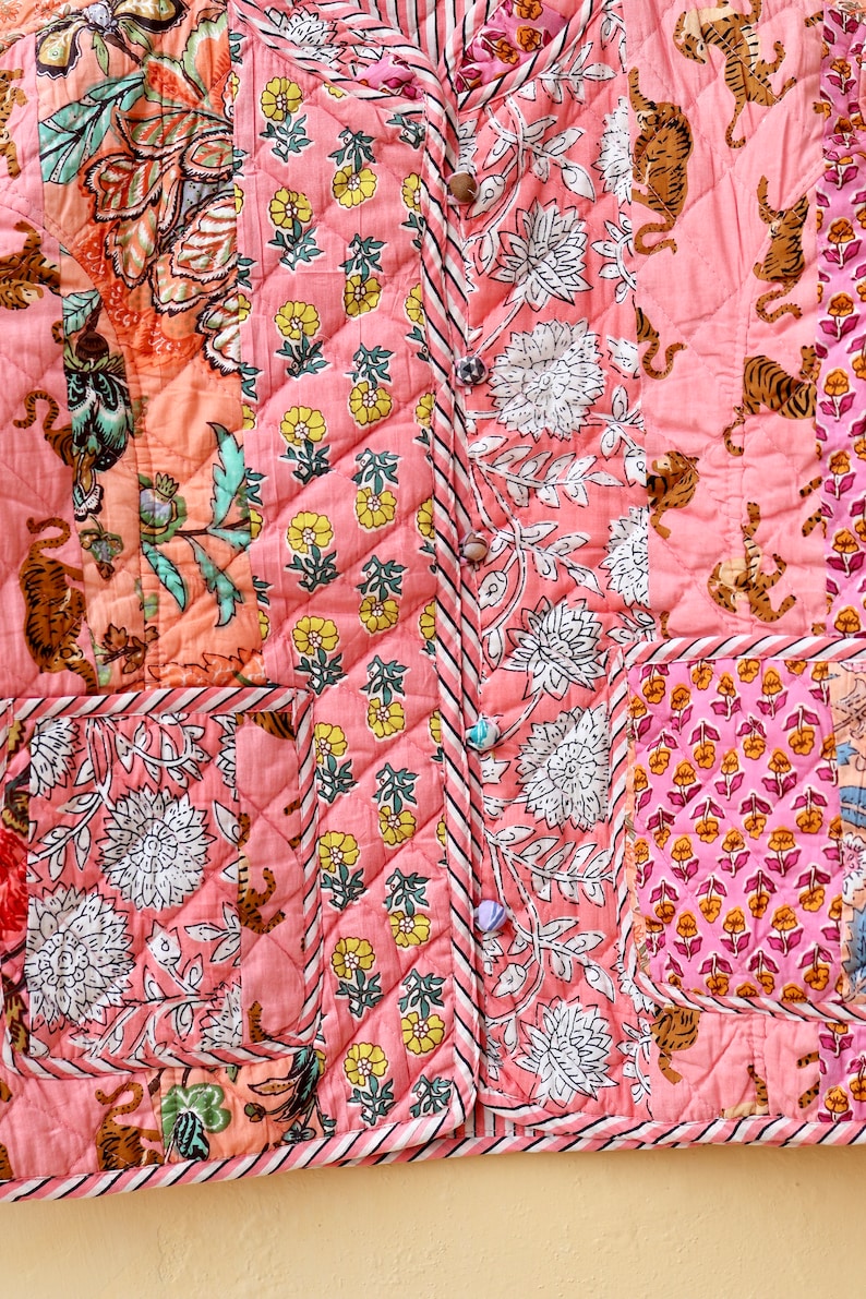 Op de afbeelding: Gewatteerde jas met een patchwork ontwerp met bloemen- en tijgerprints in roze, perzik en wit. De jas heeft een knoopsluiting en twee zakken. De algehele esthetiek is boheems en artistiek.