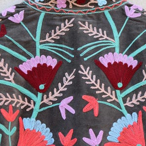 Peut inclure: Une veste en velours marron avec des broderies florales color&eacute;es. La broderie est r&eacute;alis&eacute;e avec du fil rose, rouge, bleu et vert.