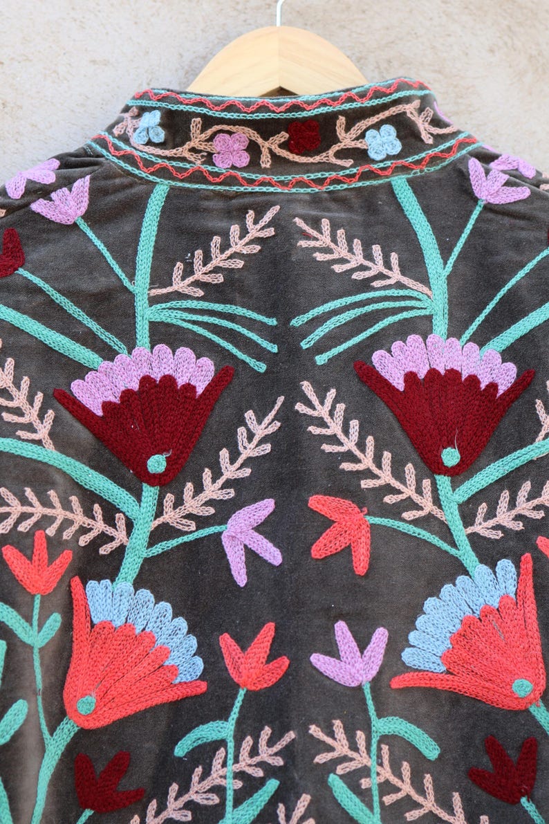 Peut inclure: Une veste en velours marron avec des broderies florales color&eacute;es. La broderie est r&eacute;alis&eacute;e avec du fil rose, rouge, bleu et vert.