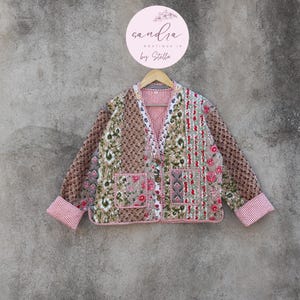 May include: A brown, white, and red patchwork jacket with floral and geometric patterns. The jacket has a V-neck and a button closure. The label on the hanger reads "sandra boutique in by stella".