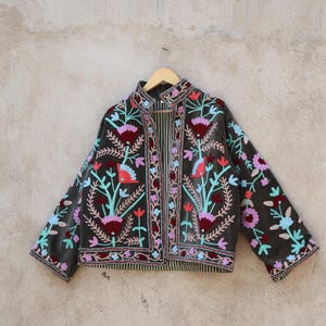 Peut inclure: Une veste en velours gris fonc&eacute; avec des broderies florales color&eacute;es. La veste a un col mandarin et une fermeture &agrave; l'avant. La broderie pr&eacute;sente des fleurs roses, bleues, vertes et rouges.