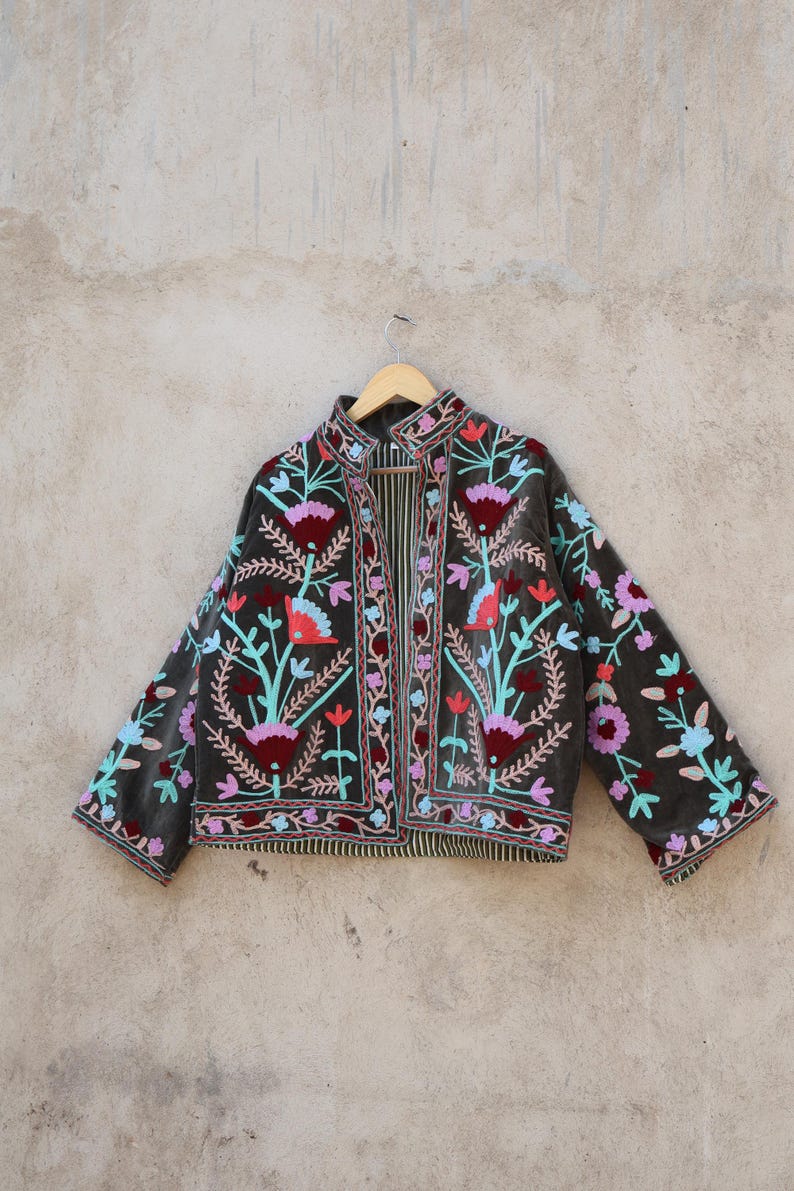 Peut inclure: Une veste en velours gris fonc&eacute; avec des broderies florales color&eacute;es. La veste a un col mandarin et une fermeture &agrave; l'avant. La broderie pr&eacute;sente des fleurs roses, bleues, vertes et rouges.