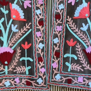 Peut inclure: Une veste en tissu gris fonc&eacute; avec un motif de broderie florale. La broderie pr&eacute;sente des fleurs et des feuilles roses, rouges, bleues et turquoise. La veste est doubl&eacute;e de rayures.