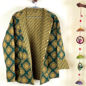 Peut inclure: Une veste réversible verte et dorée avec une fermeture à boutons et un motif géométrique. La veste est suspendue à un cintre.