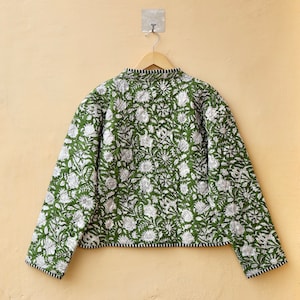 Puede incluir: Una chaqueta acolchada verde con estampado floral blanco. La chaqueta tiene un cuello mandar&iacute;n y mangas largas.
