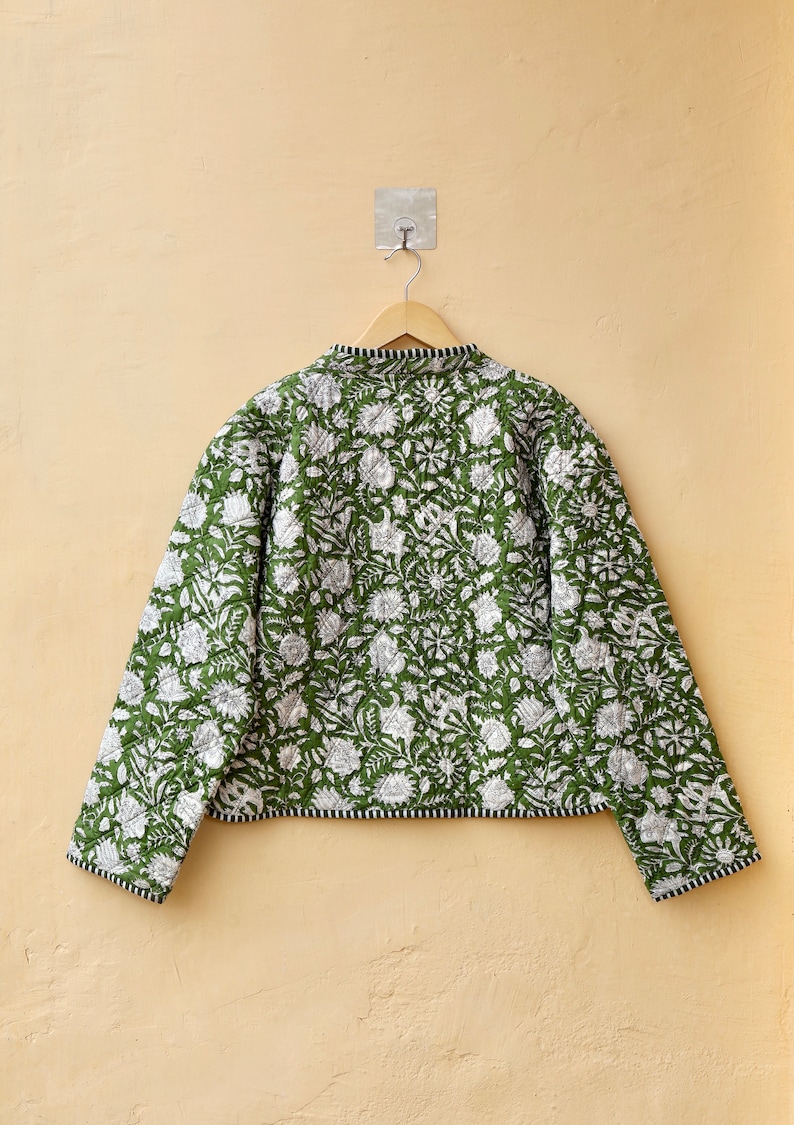 Puede incluir: Una chaqueta acolchada verde con estampado floral blanco. La chaqueta tiene un cuello mandar&iacute;n y mangas largas.