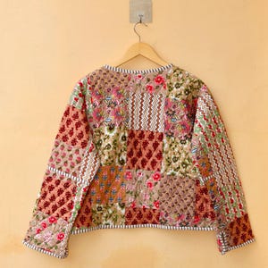 May include: A quilted jacket with a patchwork design featuring various floral patterns in shades of brown, red, and green. The jacket has long sleeves and a round neckline.