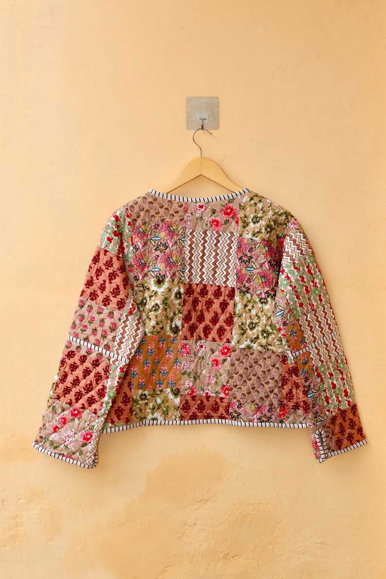 May include: A quilted jacket with a patchwork design featuring various floral patterns in shades of brown, red, and green. The jacket has long sleeves and a round neckline.