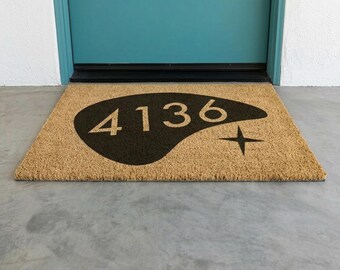 May include: A rectangular tan coir doormat featuring a large, black, amoeba-shaped graphic in the center. The graphic contains the white numbers 4136 and a four-pointed star symbol positioned to the right of the numbers on the dark background.