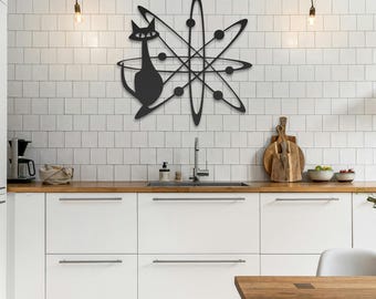 May include: A black metal wall art piece featuring a stylized cat silhouette integrated into an atomic starburst design with intersecting elliptical orbits and small circular accents, mounted on a white tiled wall above a kitchen counter.