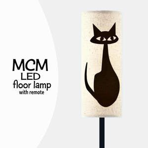 May include: A mid-century modern LED floor lamp with a black cat silhouette design. The lamp has a cylindrical shade with a cream-colored fabric and a black base. The text "MCM LED floor lamp with remote" is visible.