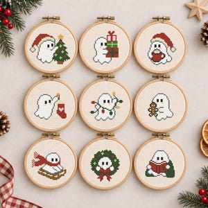 以下が含まれることがあります： クリスマスを祝う白い幽霊のクロスステッチ模様が入った9つの円形木製刺繍枠。幽霊は、ツリー、プレゼント、マグカップ、靴下、ライト、クッキー、そり、リース、本など、さまざまなクリスマスのアイテムと一緒に描かれています。