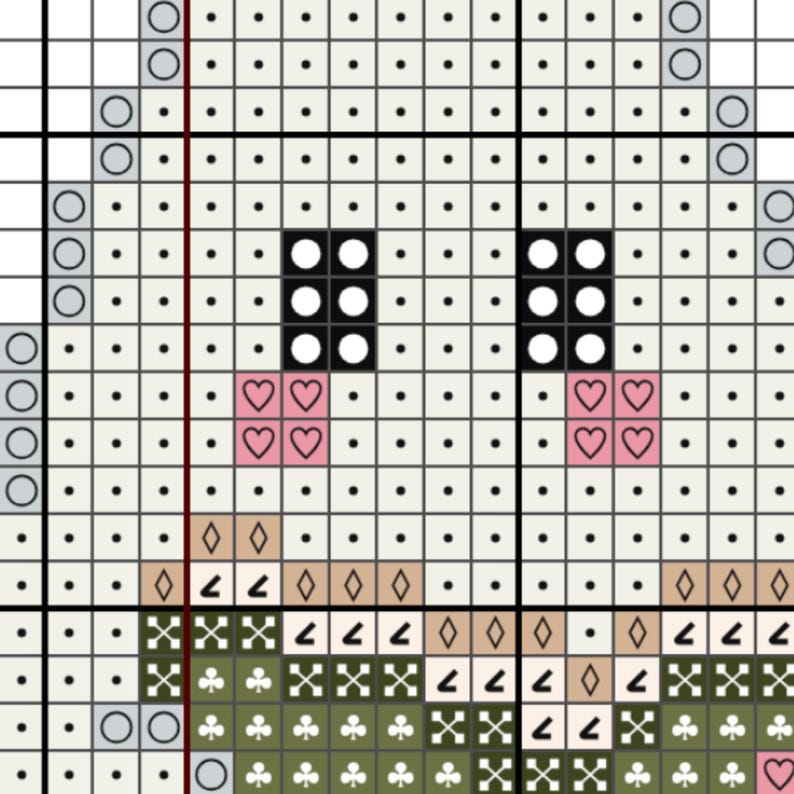 May include: A cross stitch pattern chart featuring a grid with black square eyes, pink heart-shaped cheek symbols, and a green section at the bottom. The design uses various geometric symbols like diamonds, clubs, and dots on a white background.