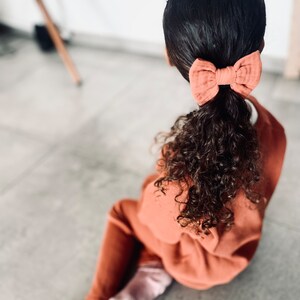 Puede incluir: Una persona joven con cabello castaño rizado que lleva un atuendo color óxido y un lazo color terracota en el cabello.