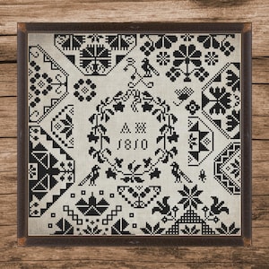 Könnte beinhalten: Gerahmtes Schwarz-Weiß-Kreuzstich-Muster mit verschiedenen geometrischen und floralen Mustern. Das Muster enthält den Text "AM 1810" in einem Kranz und ist in einem dunkelbraunen Holzrahmen gefasst.