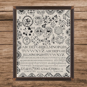 May include: Framed black and white sampler with floral and geometric patterns, letters, and numbers. The text includes "token of love 1818" and "Ann Grimshaw 1818". The sampler is in a dark brown wooden frame.