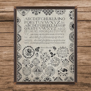 Op de afbeelding: Een ingelijste kruissteek sampler met een crèmekleurige achtergrond en zwarte steken. De sampler bevat het alfabet, cijfers en diverse bloemen- en geometrische ontwerpen. De tekst "Mary Harris" en "beloved 1821" zijn ook opgenomen.