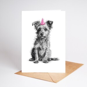 May include: A greeting card featuring a detailed pencil drawing of a small dog wearing a pink party hat with white polka dots. The dog is sitting upright, with its tail curled to the side. The card is on a brown envelope.