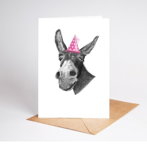 May include: A monochrome illustration of a donkey wearing a pink party hat with white hearts. The donkey is on a white card, placed on a brown envelope. The card is suitable for birthdays or celebrations.