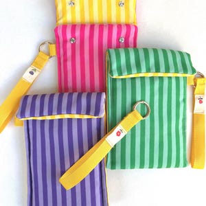 Puede incluir: Cuatro bolsas a rayas de colores, amarillo, rosa, verde y morado. Cada bolsa tiene una correa amarilla a juego con un anillo plateado y una pequeña etiqueta decorativa. Las bolsas son rectangulares con cierre de solapa y están hechas de tela.