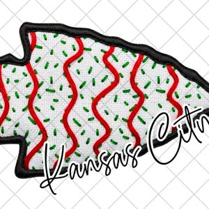 May include: Embroidered patch in the shape of an arrowhead, featuring a white background with red wavy lines and green sprinkles. The patch has a black border and the words "Kansas City" in a script font.