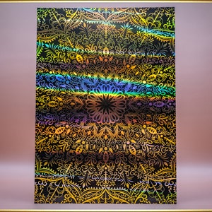 Può includere: Uno sfondo olografico con un motivo a mandala nero e oro. Il motivo è intricato e dettagliato, con un effetto arcobaleno.