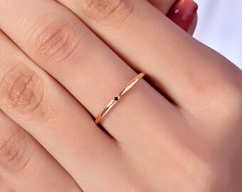 May include: A delicate rose gold band ring with a single black diamond accent.
