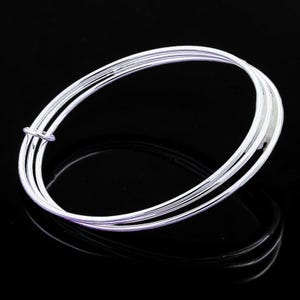 May include: A silver-toned bangle bracelet composed of three thin, interlocking circular bands. The metal has a polished, reflective surface that catches the light, creating a smooth, continuous loop design that is simple and uniform in appearance.