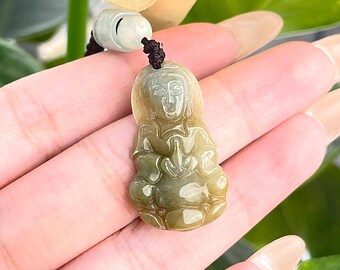 May include: A jade pendant featuring a carved figure of a person in a seated position with hands clasped in prayer. The pendant is a light green colour with a slightly yellow hue.