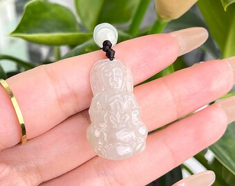 May include: White jade pendant carved in the shape of a seated figure with a serene expression. The pendant is attached to a black cord.