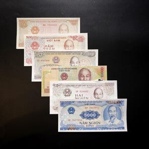 Op de afbeelding: Een verzameling van zes Vietnamese Dong-bankbiljetten gerangschikt in een trapsgewijze stapel. De biljetten hebben denominaties van 200, 500, 1000, 10000, 2000 en 5000, elk met het portret van Ho Chi Minh en de tekst Cong Hoa Xa Hoi Chu Nghia Viet Nam.