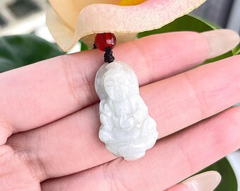 May include: White jade pendant carved with a figure of a deity, hanging from a black cord with a red bead.