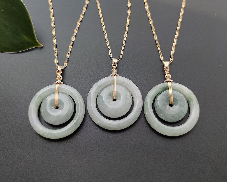 May include: Three gold-toned necklaces with jade pendants. Each pendant features a large, light green circular jade stone surrounding a smaller, matching jade circle. The pendants hang from delicate gold chains.