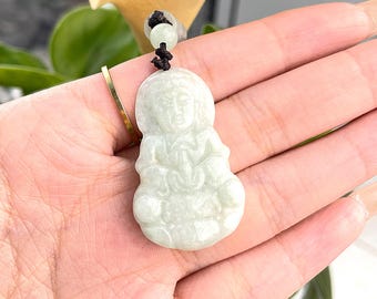 May include: A white jade pendant necklace featuring a carved figure of a woman with a serene expression. The pendant is suspended from a brown cord.