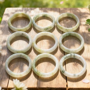 以下が含まれることがあります： 3x3のグリッド状に配置された9つの円形の翡翠のバングル。各バングルは、半透明の淡い緑色で、わずかに濃い緑色のインクルージョンがあり、滑らかで磨かれた表面と、全体を通して一貫した丸みを帯びたプロファイルが特徴です。