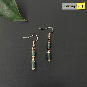 May include: Two pairs of dangle earrings with gold-colored hooks and accents. Each earring features three dark teal, rectangular beads separated by small gold-colored beads. The earrings are displayed on a dark gray background. The text "Earrings (3)" is in the upper right corner.
