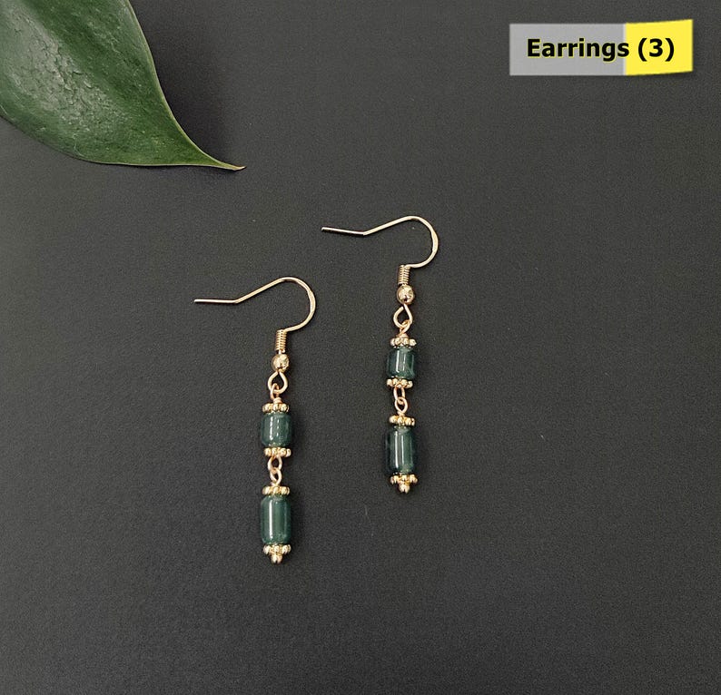 May include: Two pairs of dangle earrings with gold-colored hooks and accents. Each earring features three dark teal, rectangular beads separated by small gold-colored beads. The earrings are displayed on a dark gray background. The text "Earrings (3)" is in the upper right corner.