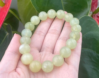 May include: A light green beaded bracelet. The bracelet is made of round, polished beads. The beads are a pale, translucent green color. The bracelet is shown against a background of green leaves and a red flower.