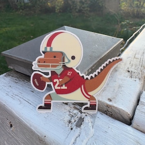 Bonita pegatina de dinosaurio jugador de fútbol. Regalo para amantes de los deportes. Ideal para portátiles, botellas de agua y cuadernos infantiles.