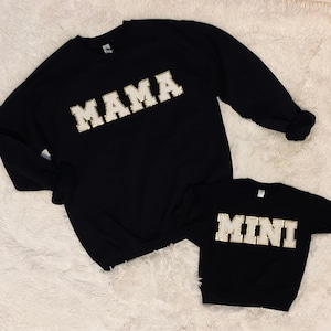 May include: Two black sweatshirts with gold glitter lettering. The larger sweatshirt says "MAMA" and the smaller sweatshirt says "MINI".