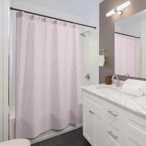 May include: A light pink and white striped shower curtain hangs in a bathroom. The curtain is suspended from a dark metal rod. The bathroom has white cabinets, a marble countertop, and a mirror.