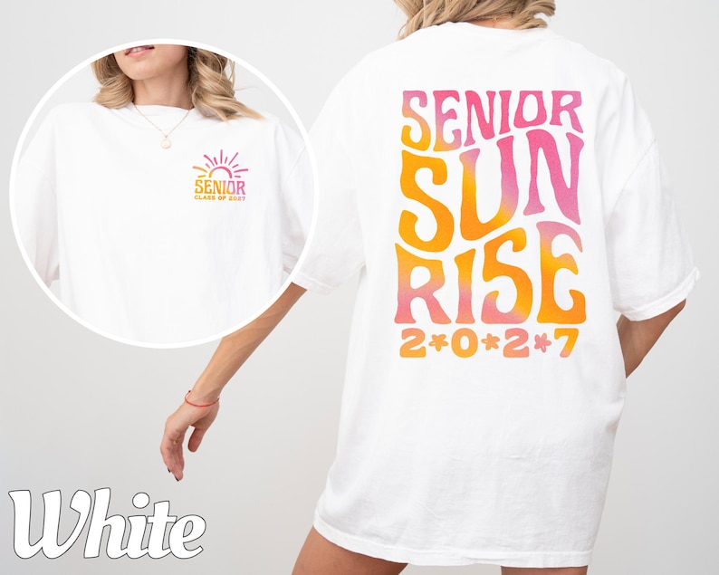 Puede incluir: Una camiseta blanca con un gr&aacute;fico grande en la espalda con el texto SENIOR SUNRISE 2*0*2*7 en una fuente ondulada con degradado de naranja a rosa. Una versi&oacute;n m&aacute;s peque&ntilde;a del mismo gr&aacute;fico est&aacute; impresa en la parte frontal izquierda.