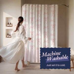 May include: White shower curtain with a repeating pink bow pattern. The bottom section has pink and white vertical stripes. The text on the image says "Machine Washable" and "Just set it to cold."