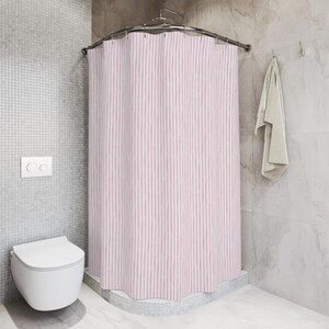 May include: A pink and white striped shower curtain hangs from a curved metal rod in a bathroom. A white toilet and a towel are also visible. The walls are a light gray color.