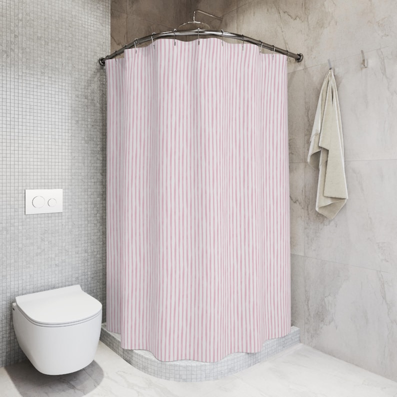 May include: A pink and white striped shower curtain hangs from a curved metal rod in a bathroom. A white toilet and a towel are also visible. The walls are a light gray color.
