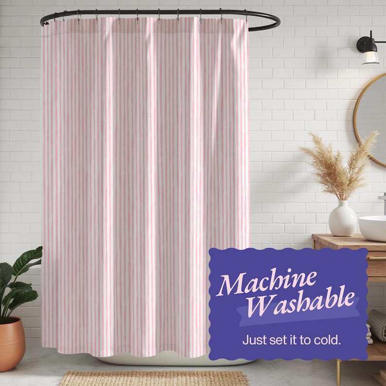 May include: A pink and white striped shower curtain hanging from a black curved rod. The text "Machine Washable" and "Just set it to cold" is visible on a blue label. The curtain is in front of a white brick wall.