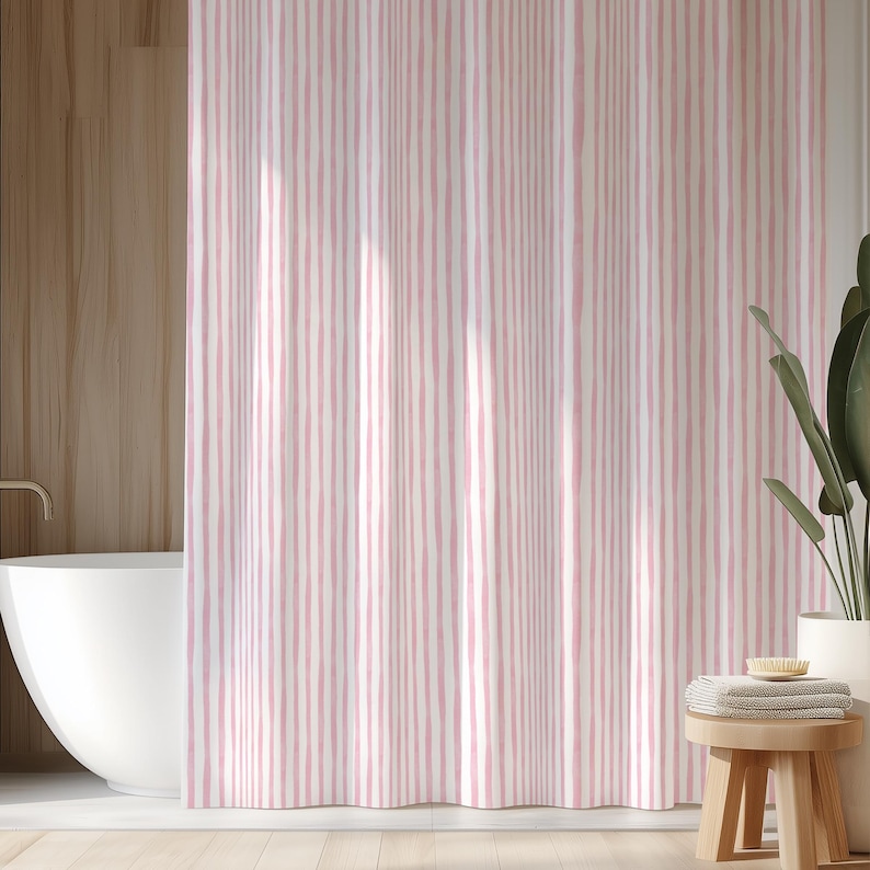 May include: A pink and white striped shower curtain hangs in front of a white bathtub. The curtain has vertical stripes of varying widths. A wooden stool with towels and a plant in a white pot are in the background.